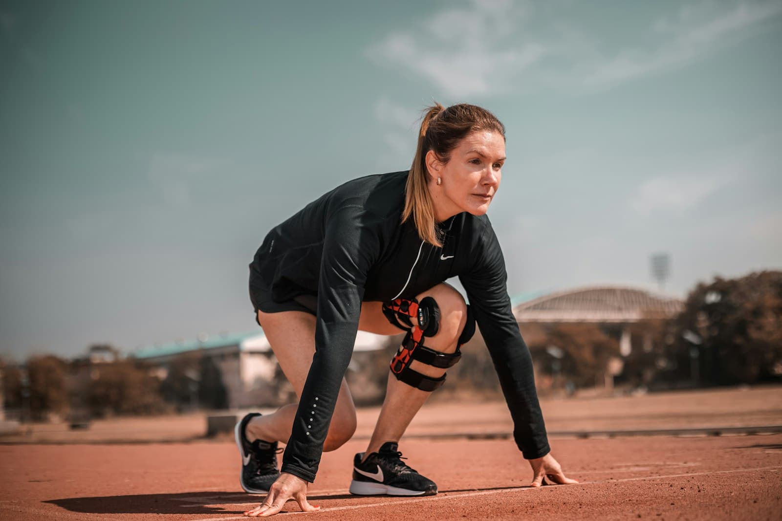 Athlete in a knee brace crouched at the start line of a track, peptides for injury recovery at PeRx